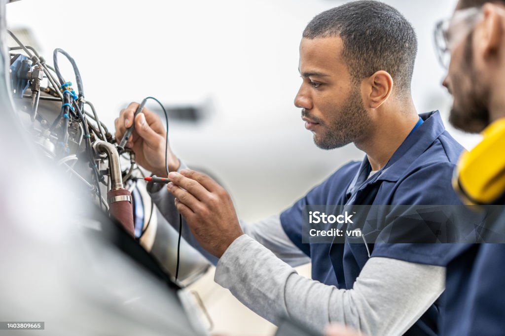 Aircraft engineers examining helicopter engine with multimeter, close up Aircraft engineers examining helicopter engine with multimeter, close up. Mechanics in uniforms working in hangar, side view Engineer Stock Photo