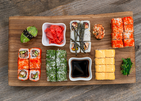 set of sushi and rolls on black tray with chopsticks on wooden table, close up