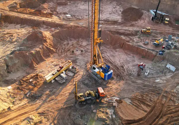 Photo of Deep foundation machine. Drilling rig and Pile driver at construction site. Pile driven into ground by vibrating hydraulic hammer.