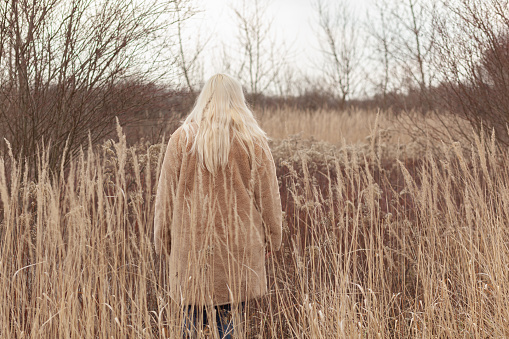 Anonymous woman with long blonde hair standing in the field, back view