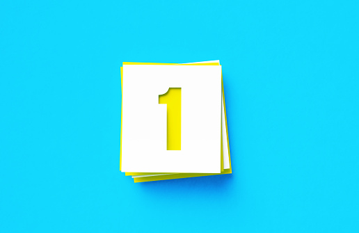 Number 1 written yellow and white adhesive notes sitting on blue background. Horizontal composition with copy space.