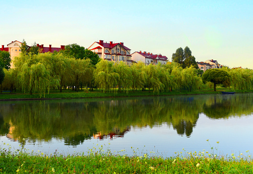 River on sunrise. Townhouses buildings and multi-floor home at waterfront. Morning on River in city. Suburb houses and residential building near river in Minsk. House in nature on shore on sunset.