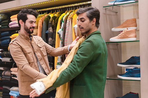 Store owner trying shirt on male customer in menswear showroom