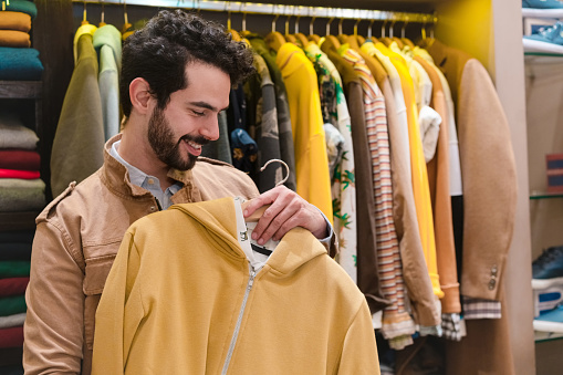 Smiling male customer holding yellow hoodie in menswear clothing store