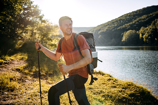 Hiker stands against big lake with trekking sticks