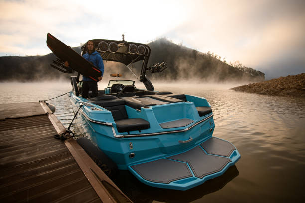 barco azul atracado no píer e um homem com uma tábua de wakeboard em suas mãos - wakeboarding motorboating extreme sports waterskiing - fotografias e filmes do acervo