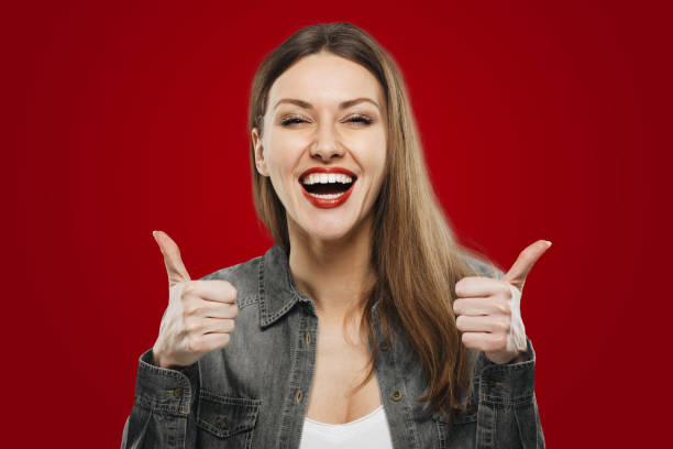 portrait d’une jeune étudiante heureuse montrant les pouces levés isolés sur fond rouge - client satisfait humour photos et images de collection