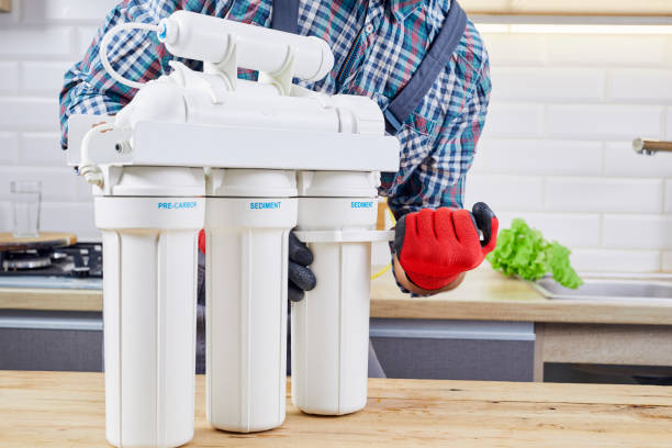 istock Plumber installs or change water filter. Replacement aqua filter. Repairman installing water filter cartridges in kitchen. Installation of reverse osmosis water purification system. 1403828437