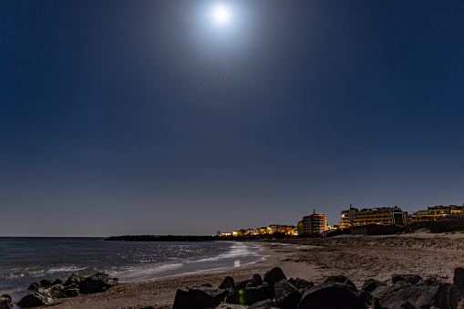 Seaside resort calm town of Pomorie with bright electric lights and large comfortable luxury hotels against background of night starry blue sky and calm cold Black Sea, in warm country of Bulgaria