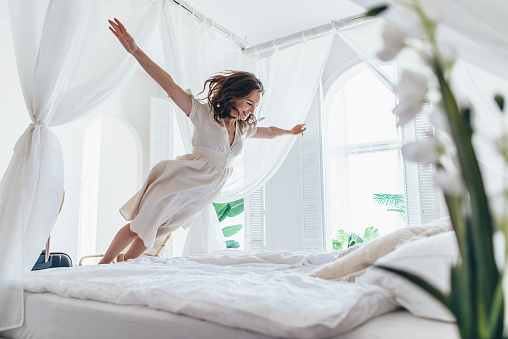 Woman jumps on the bed as if in flight.
