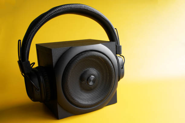 istock Black one-way audio speaker and wireless headphones with ear pads on a yellow gradient background. Concept of pop music, audio podcasts and broadcast. Free space for an inscription 1403833089