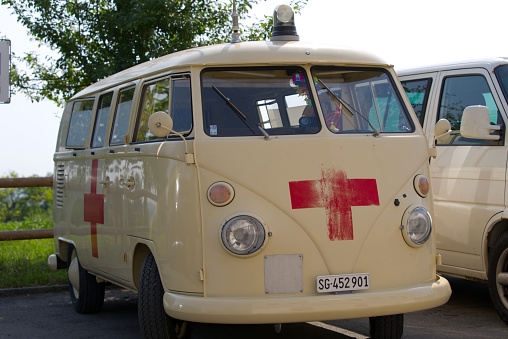 Ochre classic ambulance car VW Bus with red cross and blue light at car park at City of Zürich on a sunny hot summer day. Photo taken June 19th, 2022, Zurich, Switzerland.