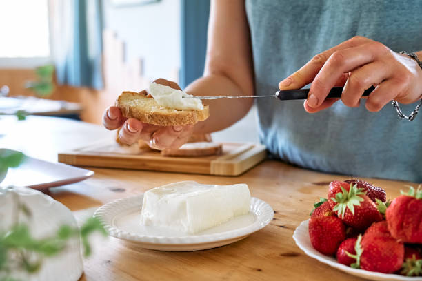 женщина готовит летний бутерброд с клубникой. женские руки намазывают сыр страчкино на хлеб для тостов. здоровое питание, бранч на фруктовы - cream cheese стоковые фото и изображения