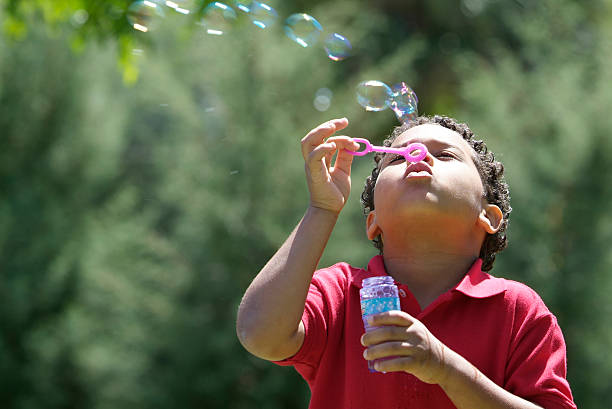 Young boy blowing bubbles outdoors at the park stock photo