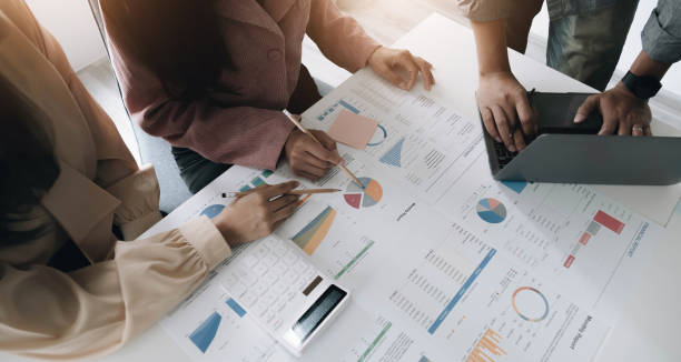 Business People Meeting using laptop computer, calculator,notebook,stock market chart paper for analysis Plans to improve quality next month. Conference Discussion Corporate Concept