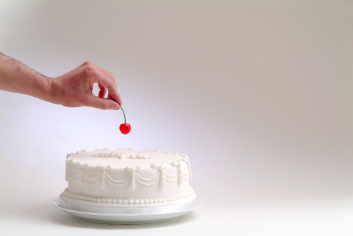 hand putting a cherry on top of a white cake