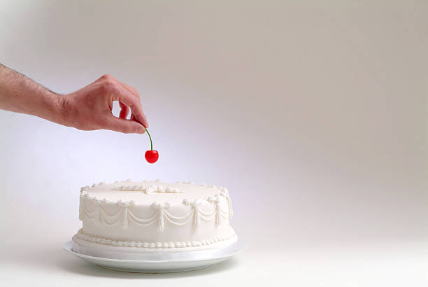 hand and cherry hand putting a cherry on top of a white cake cake stock pictures, royalty-free photos & images