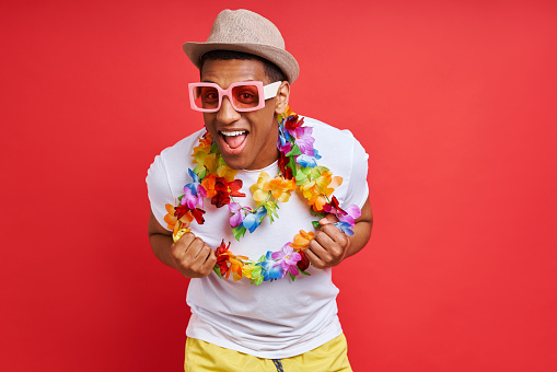 Handsome young man in Hawaiian necklace smiling while standing against red background