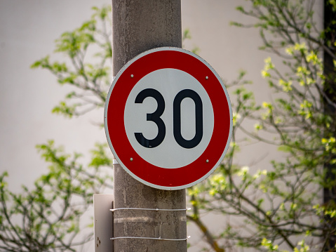30 speed limit sign on a solid light post. German speed limit in a city. Rules for the road users. The traffic speed must not be faster as 30 kilometers per hour. The road sign restricts the freedom.