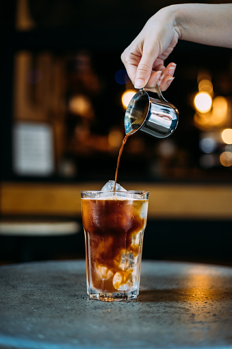 Pouring espresso shot over ice cubes for making iced americano