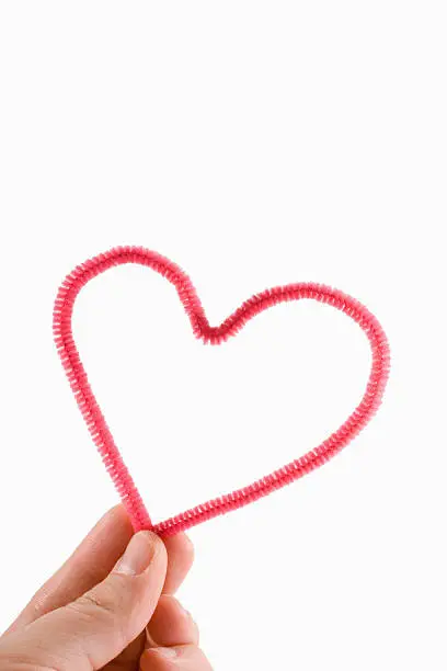 hand holding a pink heart made of pipecleaner