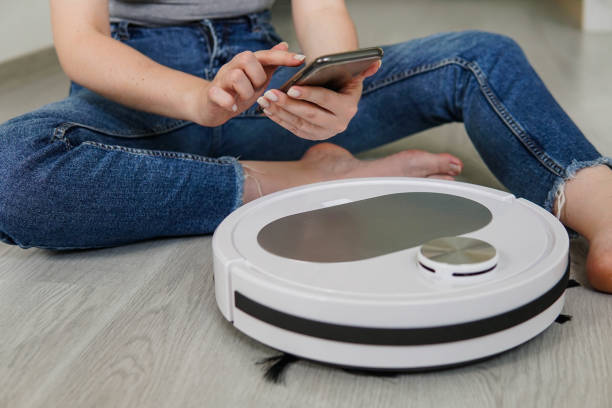 istock Woman housewife using mobile application to control robotic vacuum cleaner for start cleaning. Smart home concept. 1403843358