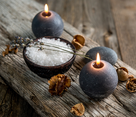Round wax burning candles and sea salt with lavender twigs on wooden background. Still life of relaxing spa treatment.