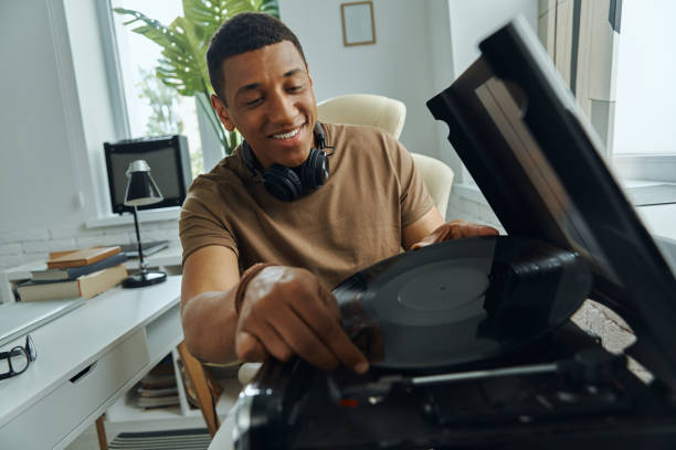 istock Cheerful young multiracial man putting vinyl record on turntable 1403846689
