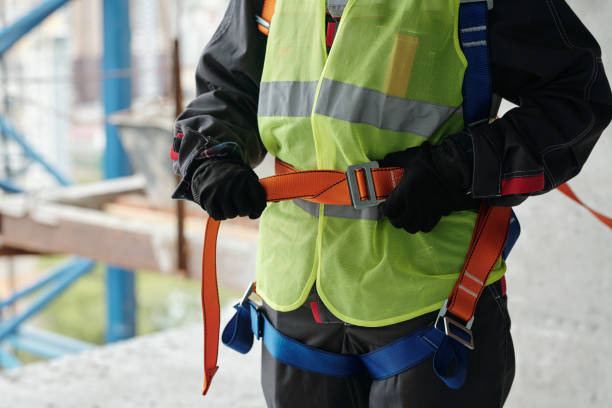 istock Young builder in hardhat, gloves and reflective vest fastening safety belt 1403846853