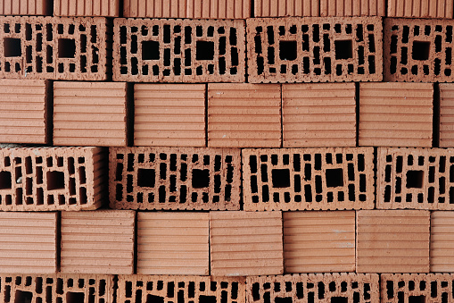 Stack of red solid clay bricks formed by several layers prepared for building work while making background or wallpaper