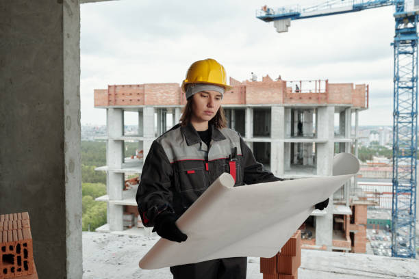 istock Young female worker with blueprint standing inside unfinished construction 1403847015