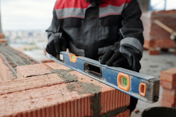 istock Gloved hands of constructor in workwear holding level on surface of brick wall 1403847047