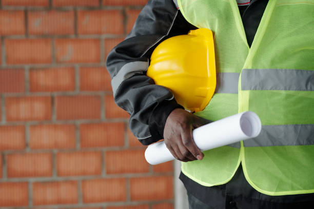 istock Midsection of foreman in reflective jacket holding hardhat and blueprint 1403847140