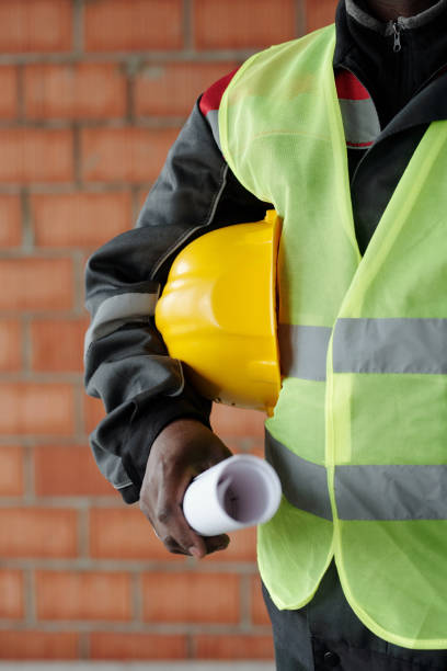 istock Part of modern foreman in reflective jacket holding hardhat and blueprint 1403847142