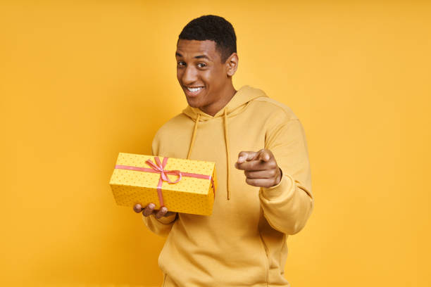 istock Cheerful mixed race man holding a gift box and pointing 1403847377