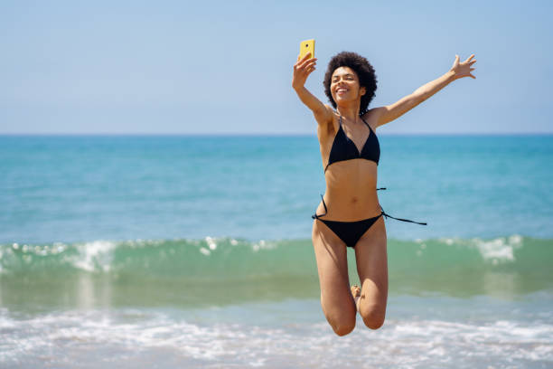 istock Happy black woman taking selfie while jumping on coast 1403847977