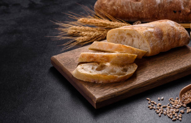 französisches baguettebrot in scheiben geschnitten auf einem holzschneidebrett vor dunklem betonhintergrund - baguette stock-fotos und bilder