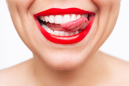 Cropped shot of young caucasian woman showing tongue and demonstrating the even teeth isolated on a white background. Perfect smile with red lipstick. Teeth whitening. Oral hygiene, dental health care
