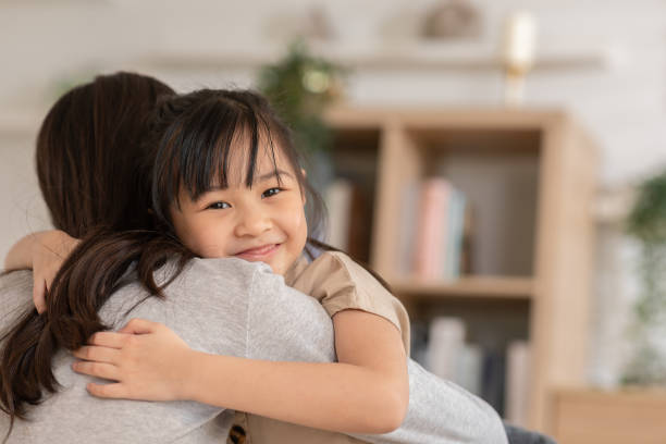 uma garota asiática abraça sua mãe pela frente e ela também sorri. as crianças se sentem tão felizes com seu momento que passaram juntos. uma mente forte poderia ser construída a partir de uma família forte. conceito de família da felicidade - seguro de vida - fotografias e filmes do acervo