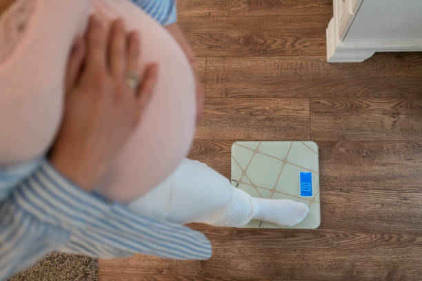 беременная женщина стоит на весах дома, крупным планом - human pregnancy rubbing looking down abdomen стоковые фото и изображения