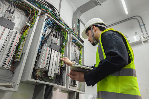 Electrical Engineer team working front control panel, An electrical engineer is installing and using a tablet to monitor the operation of an electrical control panel in a factory service room.