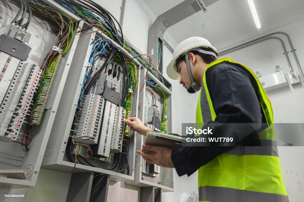 Electrical Engineer team working front control panel, An electrical engineer is installing and using a tablet to monitor the operation of an electrical control panel in a factory service room. - Royalty-free Eletricidade Foto de stock Electrical Engineer team working front control panel, An electrical engineer is installing and using a tablet to monitor the operation of an electrical control panel in a factory service room. - Royalty-free Eletricidade Foto de stock