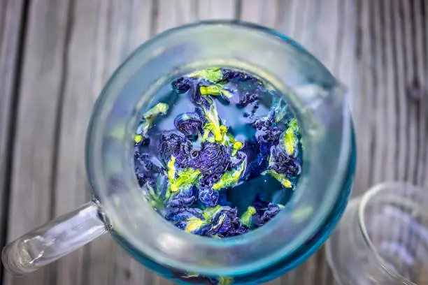 Photo of Butterfly pea blue Clitoria ternatea flowers colorful color tea flat top lay above macro closeup view in teapot on wooden table background showing detail and texture