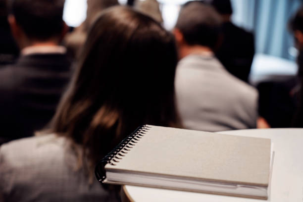 istock Notebook on a table - people sitting and attending a conference seminar 1403860653