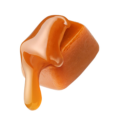 Caramel sauce flowing on caramel cube isolated on white background. Caramel candy with liquid caramel.