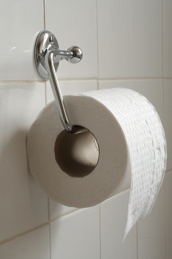 A white toilet roll on a chrome holder, white tiles