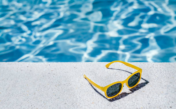 rückansicht einer gelben brille am weißen rand eines schwimmbades mit bläulichem wasser im hintergrund. konzept von urlaub und sommer. - sommer stock-fotos und bilder