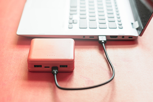 Close-up, side view of a power bank connected to a laptop, on a red background.