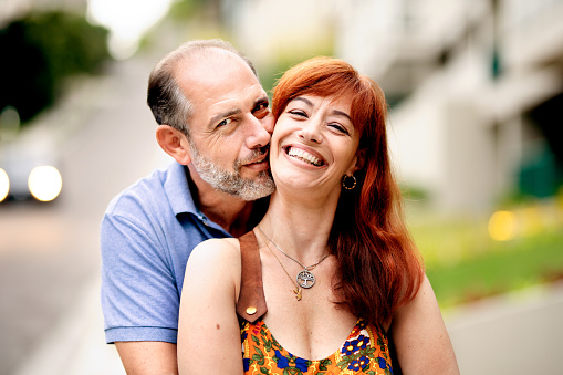 Portrait of an affectionate mature man hugging his smiling wife from behind while standing together outside in summer