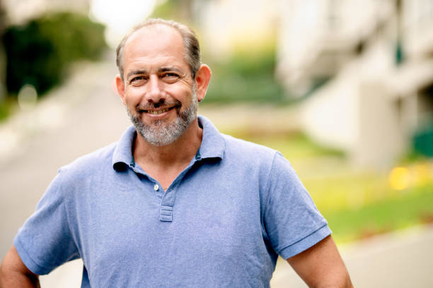 Mature man smiling while standing outside in the summertime Portrait of a mature man smiling confidently while standing with his hands on his hips outside on a sidewalk in summer mature men stock pictures, royalty-free photos & images